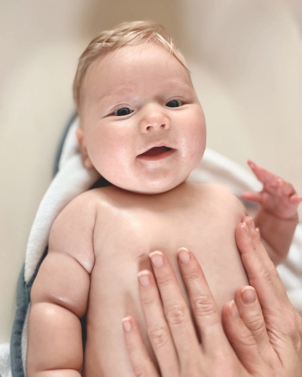 Glimlachende baby tijdens een babymassage, met de handen van de masseur op het buikje